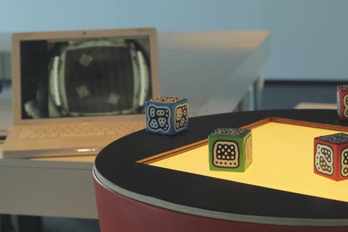 The "TRUC". In the background, the laptop displays what is seen by a camera placed inside the machine, capturing the symbol on the bottom of each cube and its position on the surface.